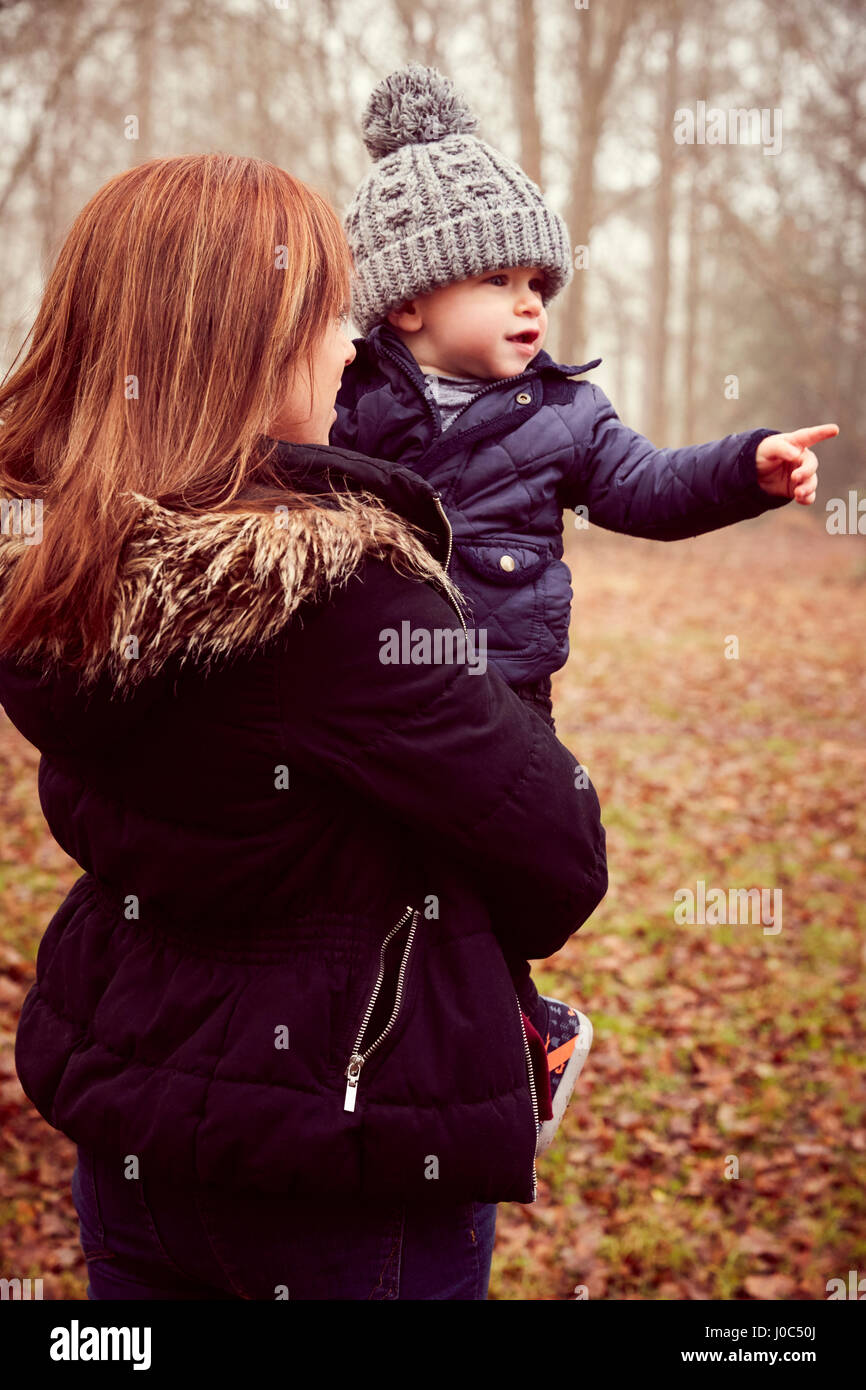 Mid adult woman carrying toddler son pointing in autumn forest Stock