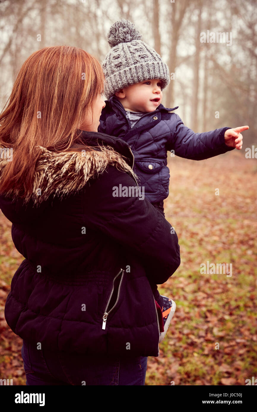 Mid adult woman carrying toddler son pointing in autumn forest Stock Photo