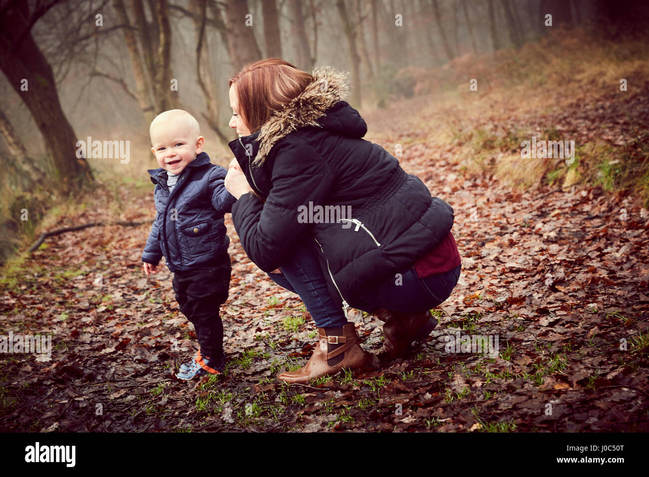 Mid adult woman crouching with toddler son in autumn forest Stock Photo