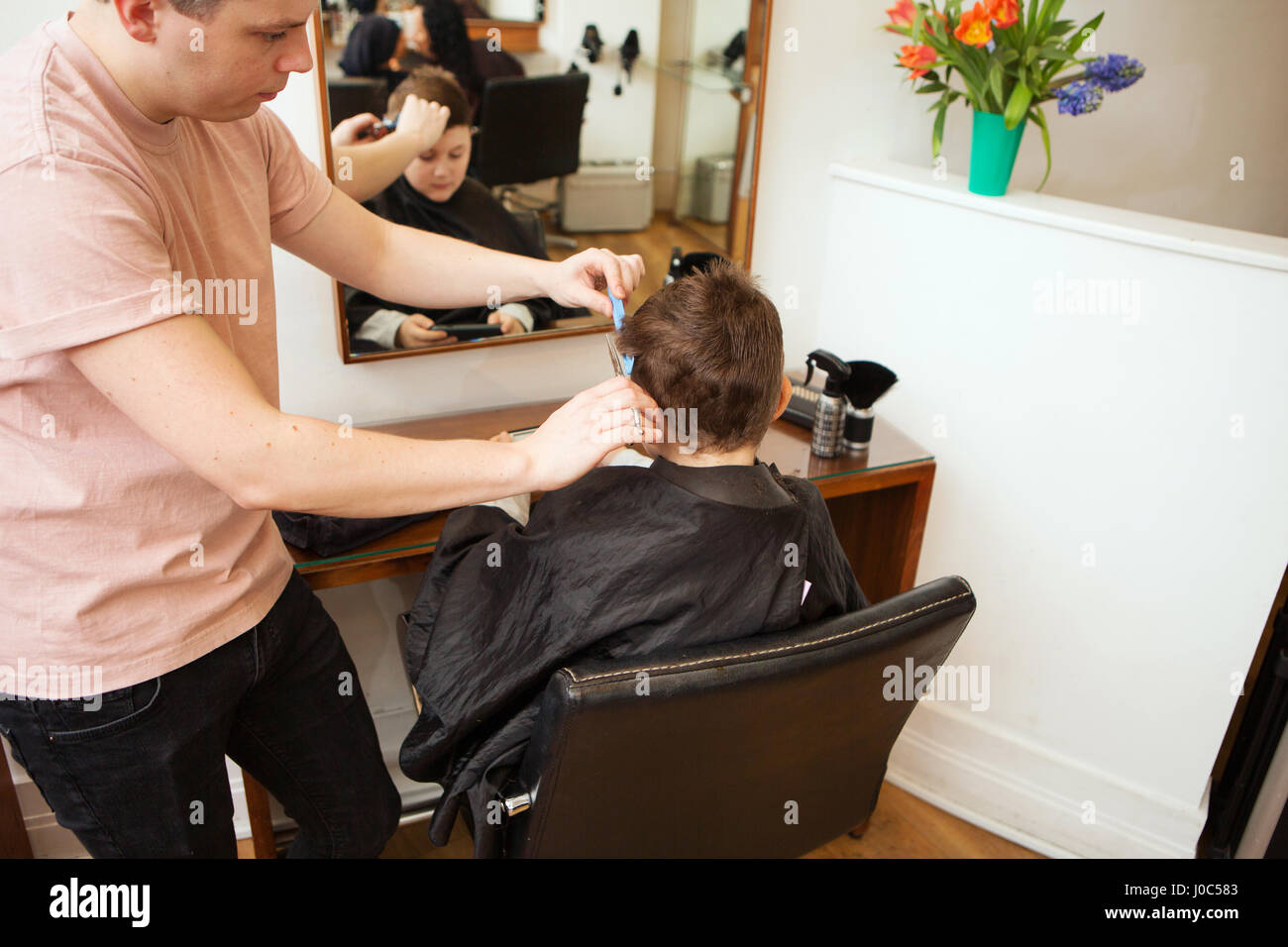 Male hairdresser trimming boy's hair in hair salon Stock Photo