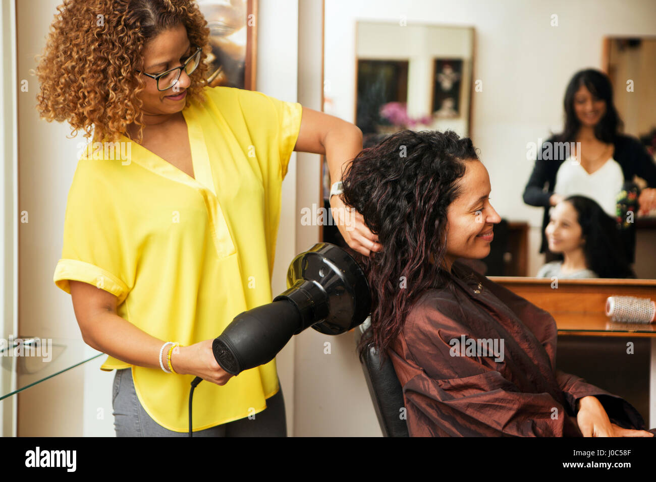 Hairdresser blow drying female customer's hair in hair salon Stock Photo