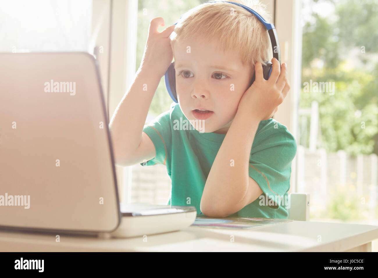 Boy at desk using laptop and listening to headphones Stock Photo