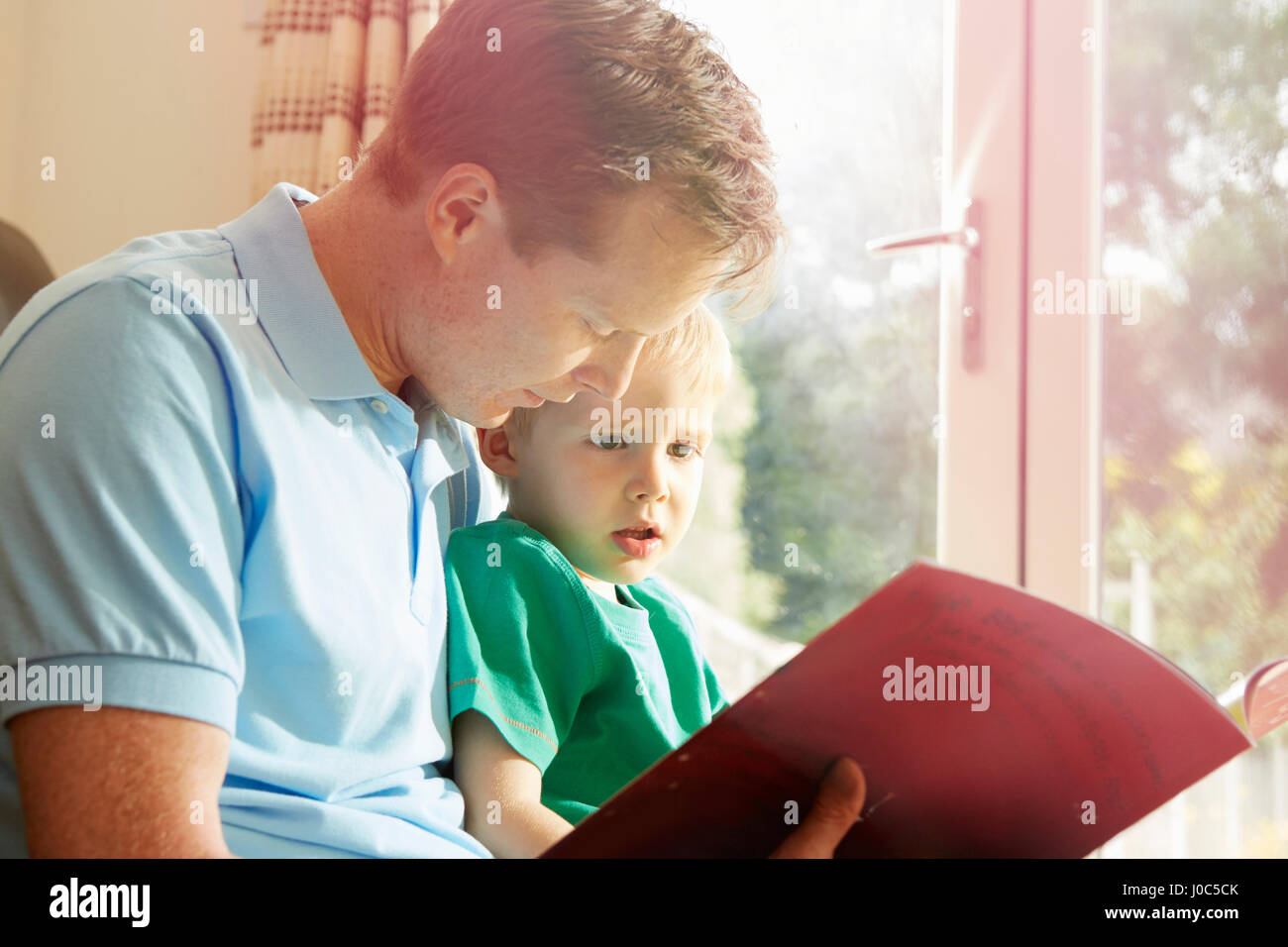 Mature man reading book to son on his lap Stock Photo