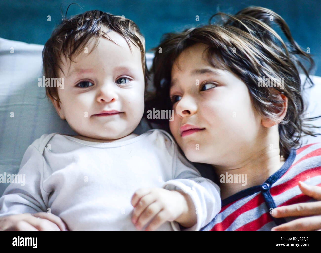 Portrait of boy lying in bed looking sideways at baby brother Stock Photo