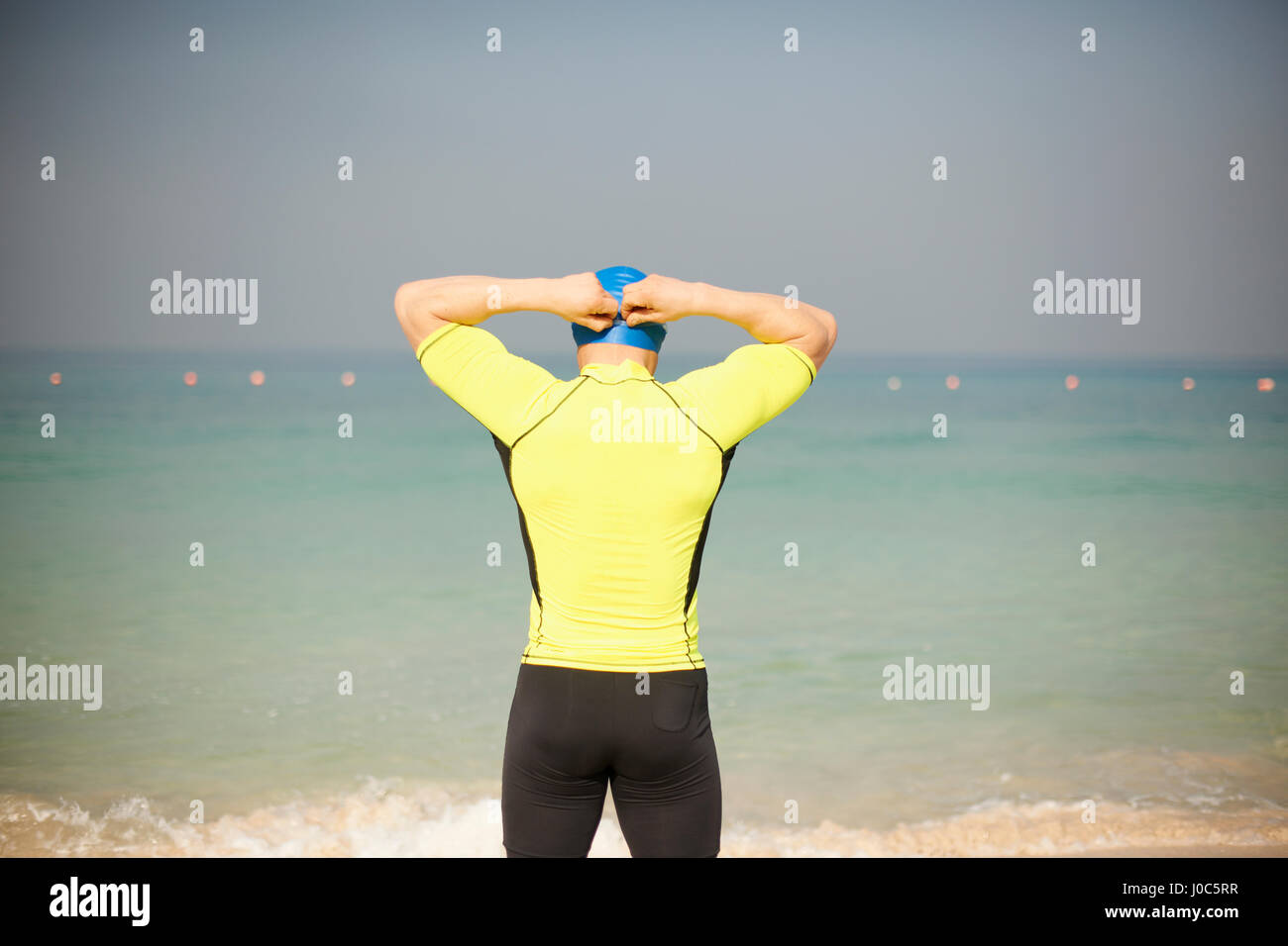 Rear view of mature man adjusting swimming cap on beach, Dubai, United Arab Emirates Stock Photo