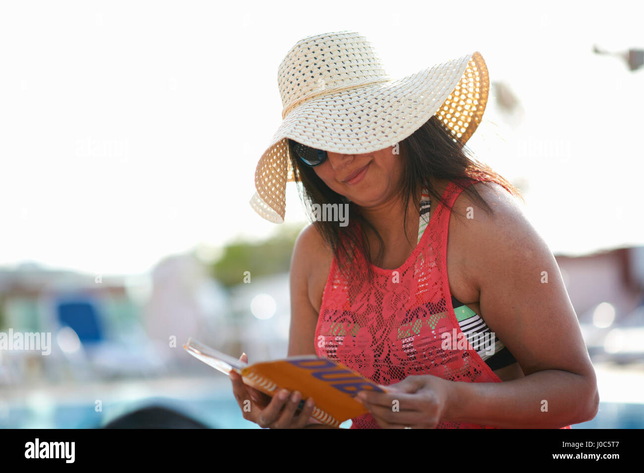 Mature woman sitting at pool side reading guidebook, Dubai, United Arab Emirates Stock Photo