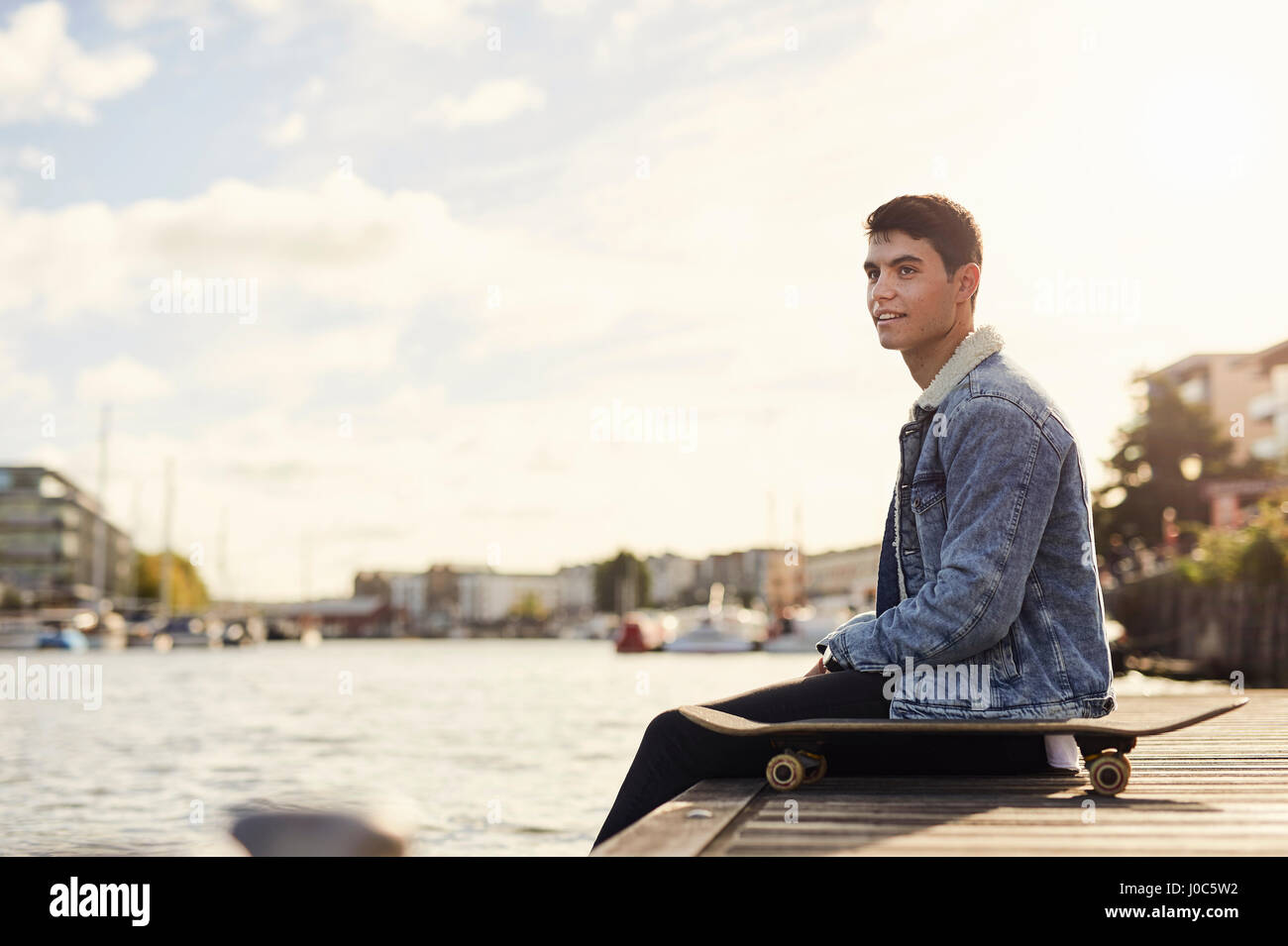 Young man sitting by river, skateboard beside him, Bristol, UK Stock Photo