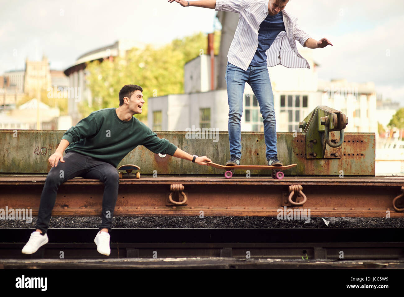 Two young men fooling around by train track, balancing on skateboard Bristol, UK Stock Photo