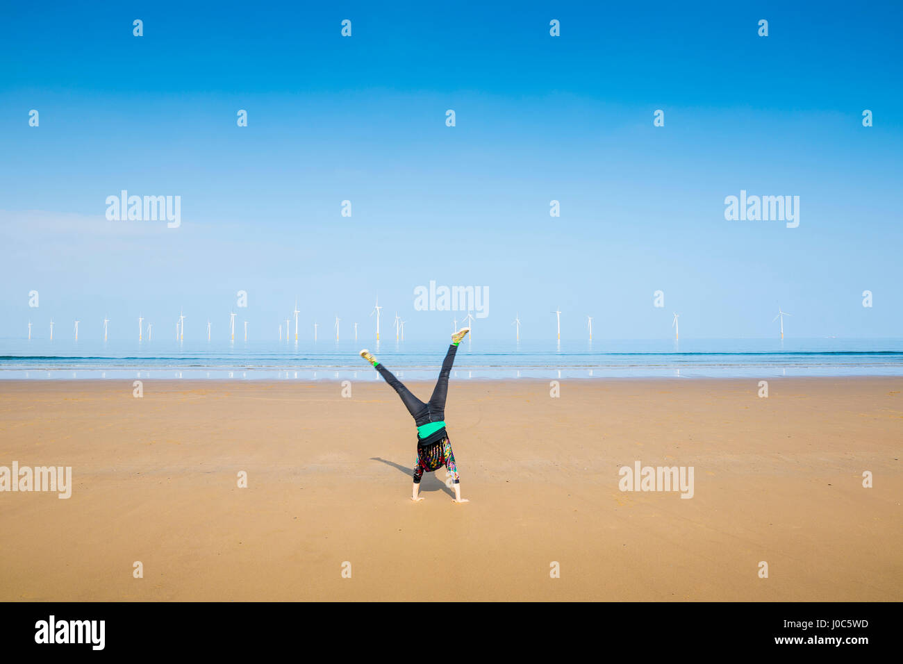 Mature woman doing cartwheel on Redcar beach, North Yorkshire, UK Stock Photo