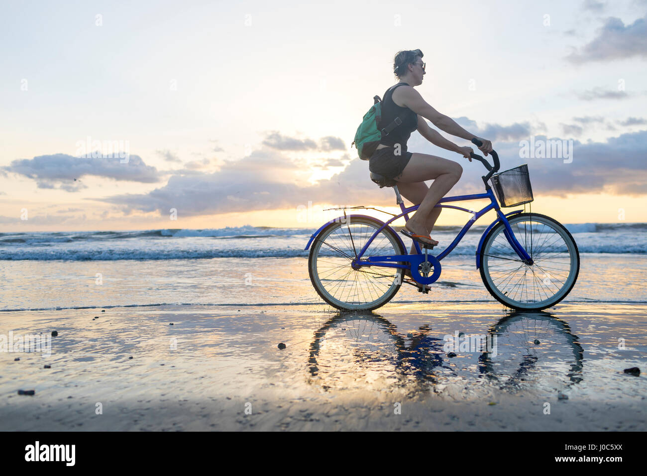 Woman cycling on beach at sunset, Nosara, Guanacaste Province, Costa Rica Stock Photo