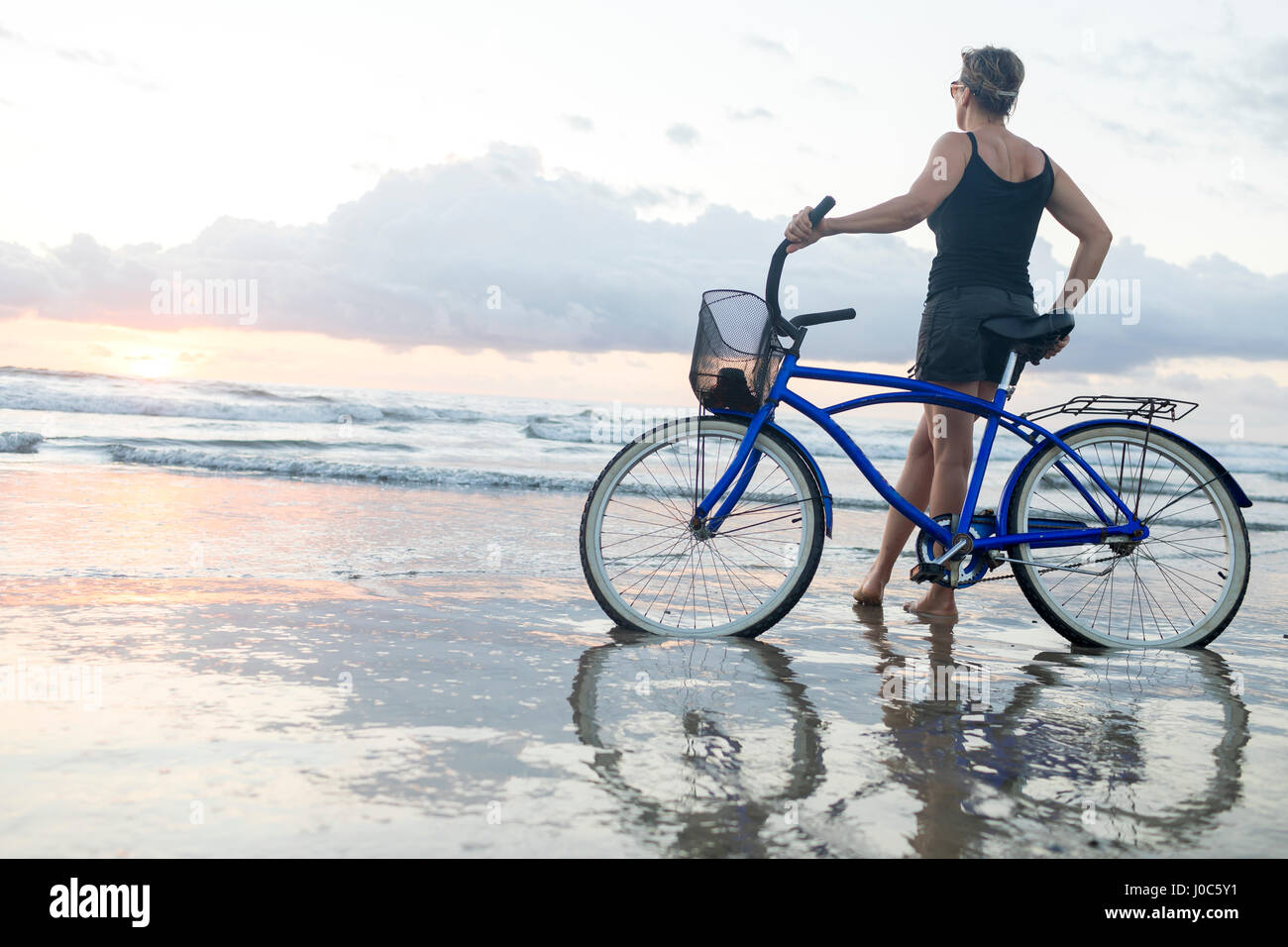 Woman with bicycle looking out from beach at sunset, Nosara, Guanacaste Province, Costa Rica Stock Photo