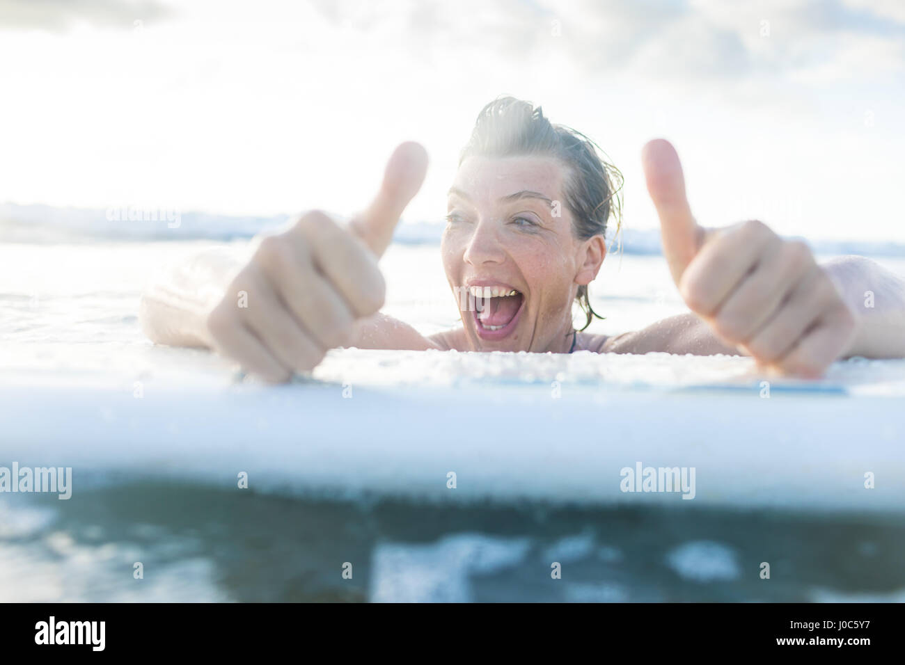 Woman with surfboard in sea giving thumbs up, Nosara, Guanacaste Province, Costa Rica Stock Photo