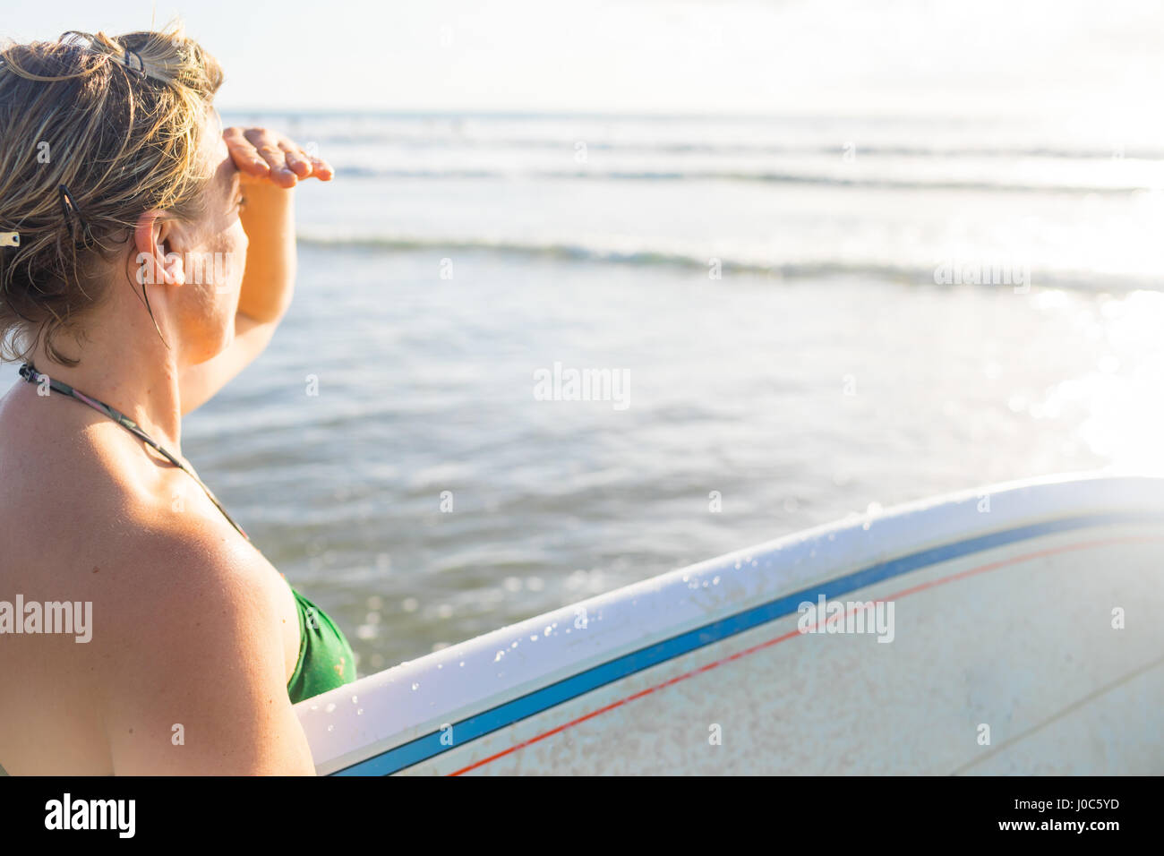 Woman carrying surfboard looking out to sea from beach, Nosara, Guanacaste Province, Costa Rica Stock Photo
