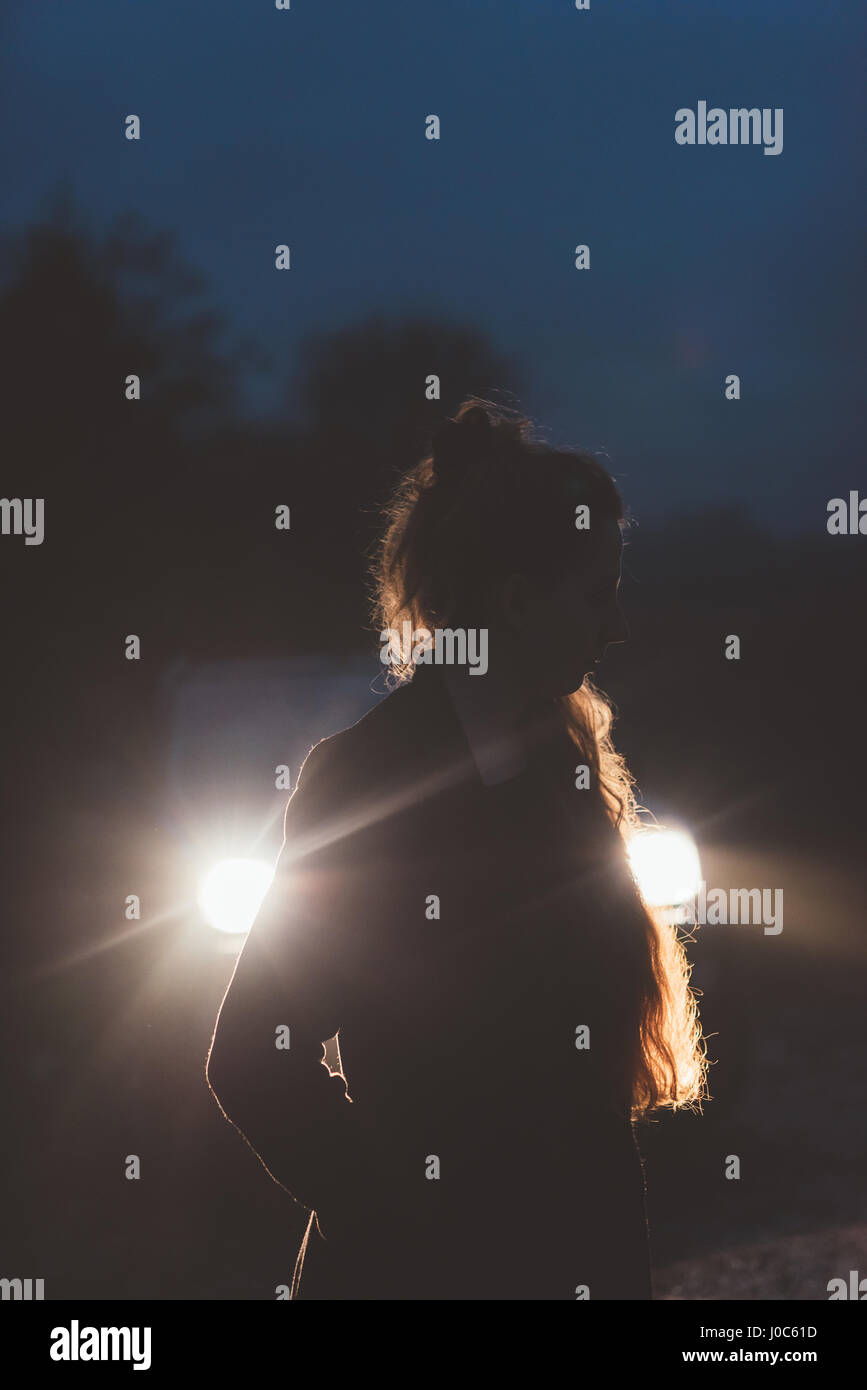 Woman in front of car headlights on roadside at night Stock Photo