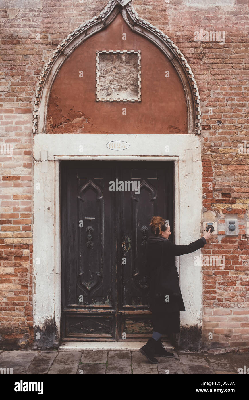 Young woman ringing doorbell of old building, Venice, Italy Stock Photo