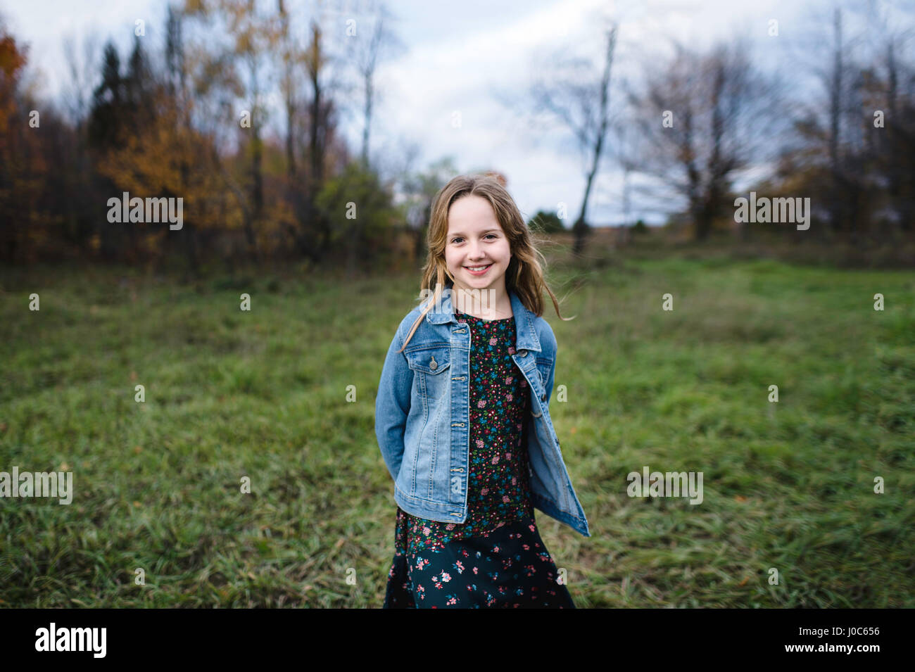 Young girl smiling in field in denim jacket, Lakefield, Ontario, Canada Stock Photo