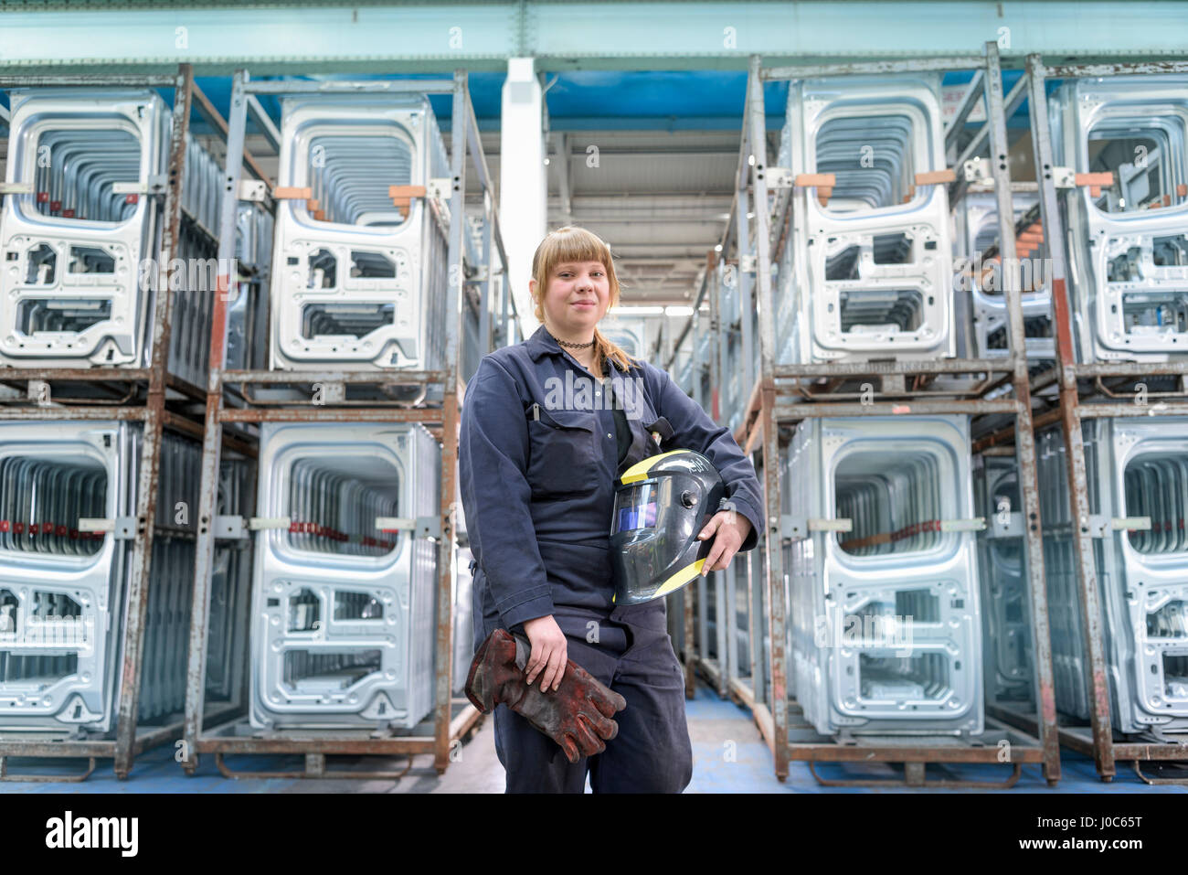 Female apprentice welder holding equipment in car factory, portrait Stock Photo
