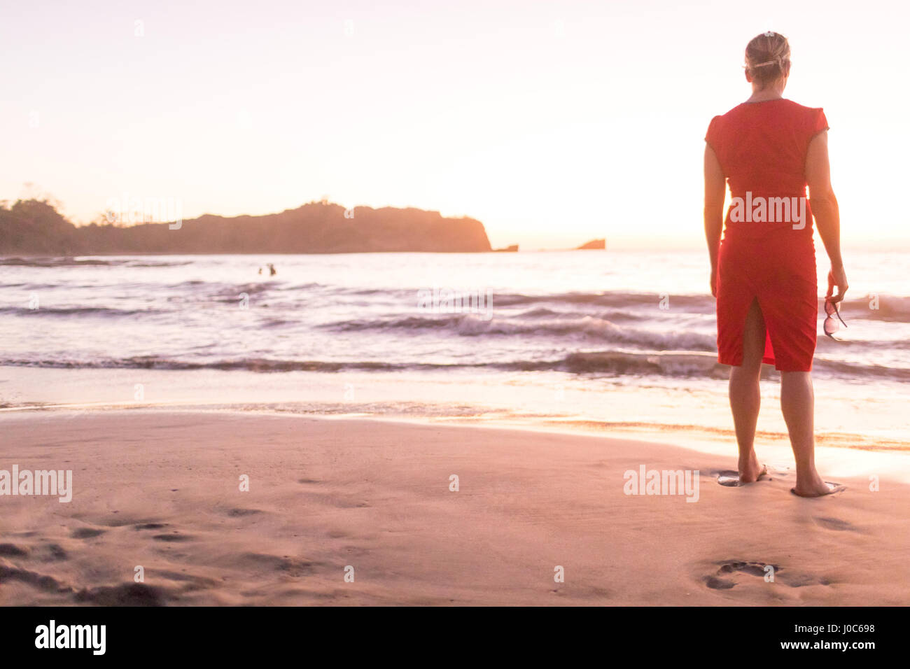 Rear view of woman looking out to sea from beach at sunset, Nosara, Guanacaste Province, Costa Rica Stock Photo