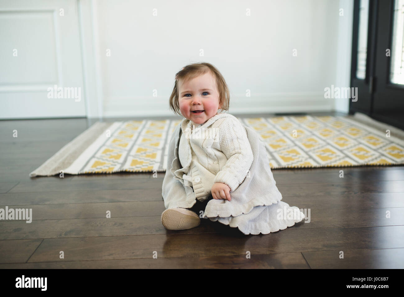 Rosy-cheeked baby sitting on the floor smiling Stock Photo
