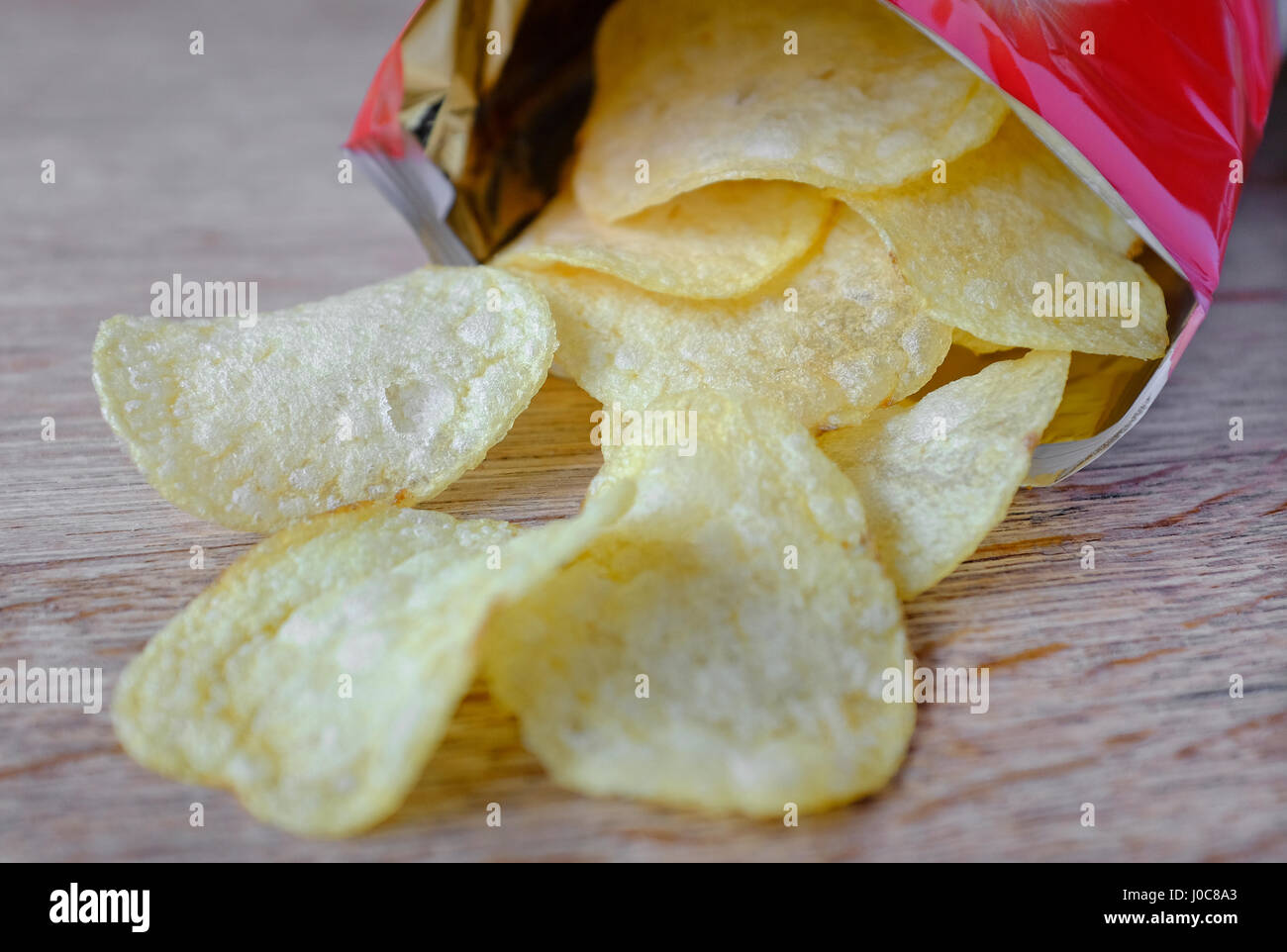 opened bag of potato crisps on wooden table top Stock Photo