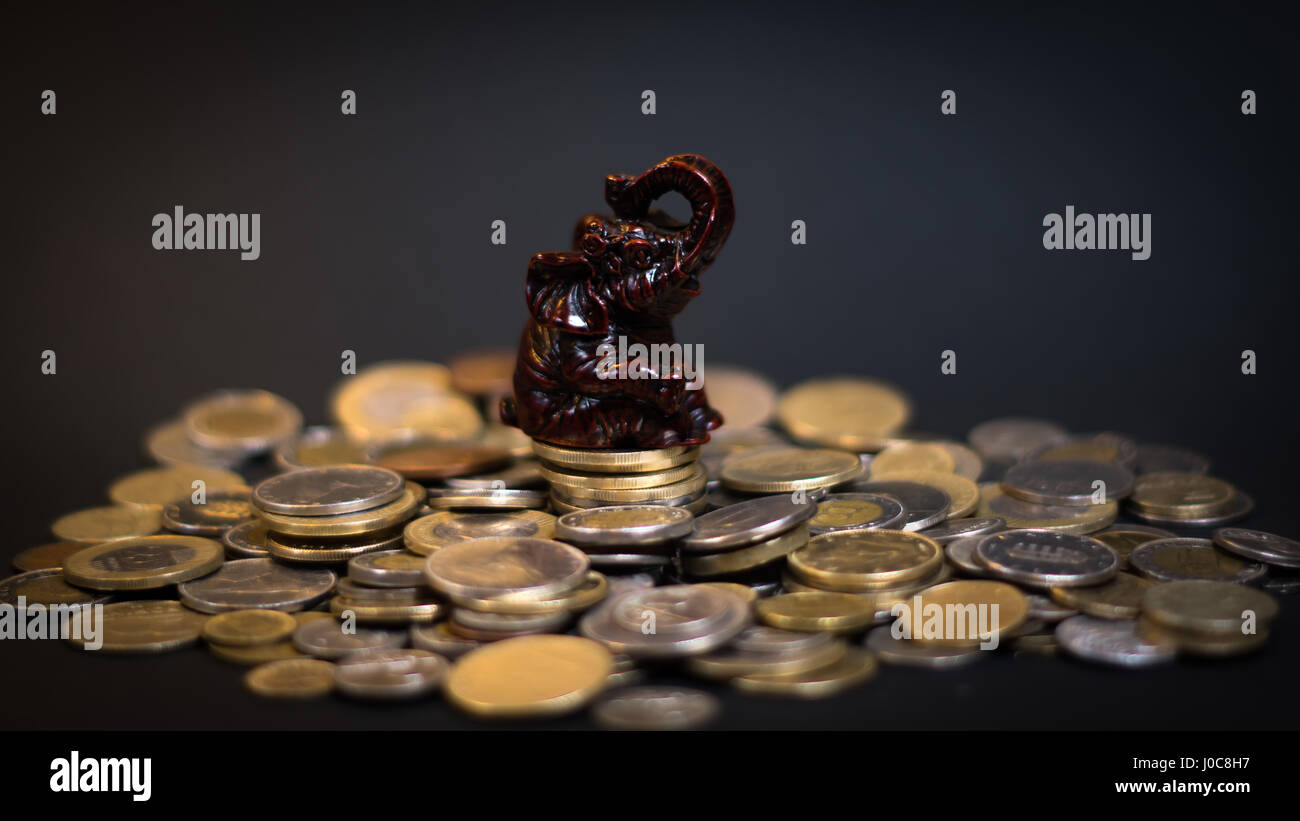 Little elephant statue sitting on a big pile of coins bringing good luck Stock Photo