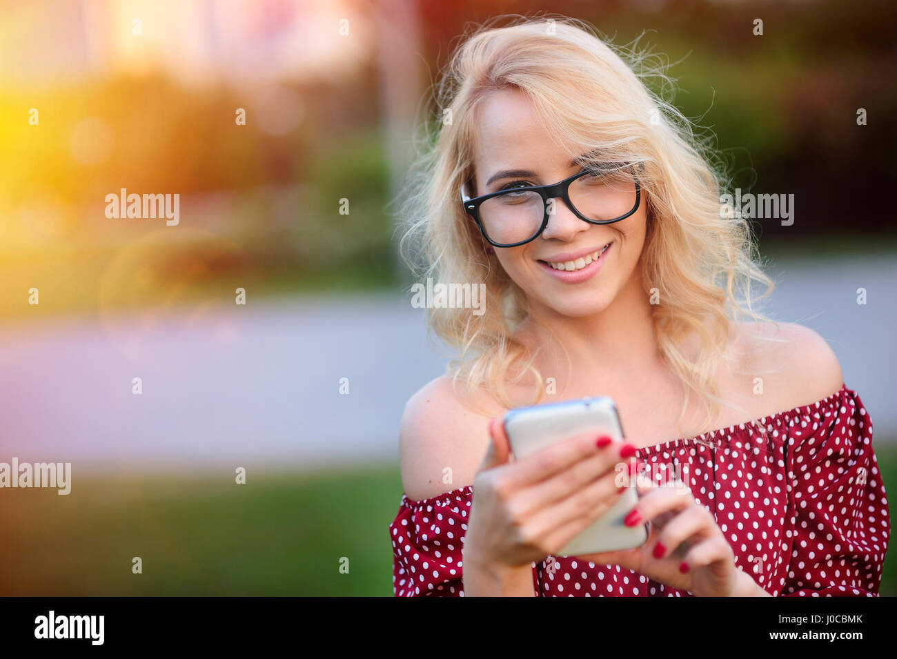 Smiling young woman in glasses with the phone outdoors Stock Photo