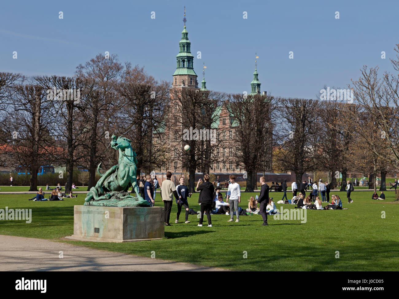 Young people enjoy the warm spring sun on Palm Sunday in Kongens Have, the King's garden, Copenhagen, Denmark. The Rosenborg Castle in the background. Stock Photo