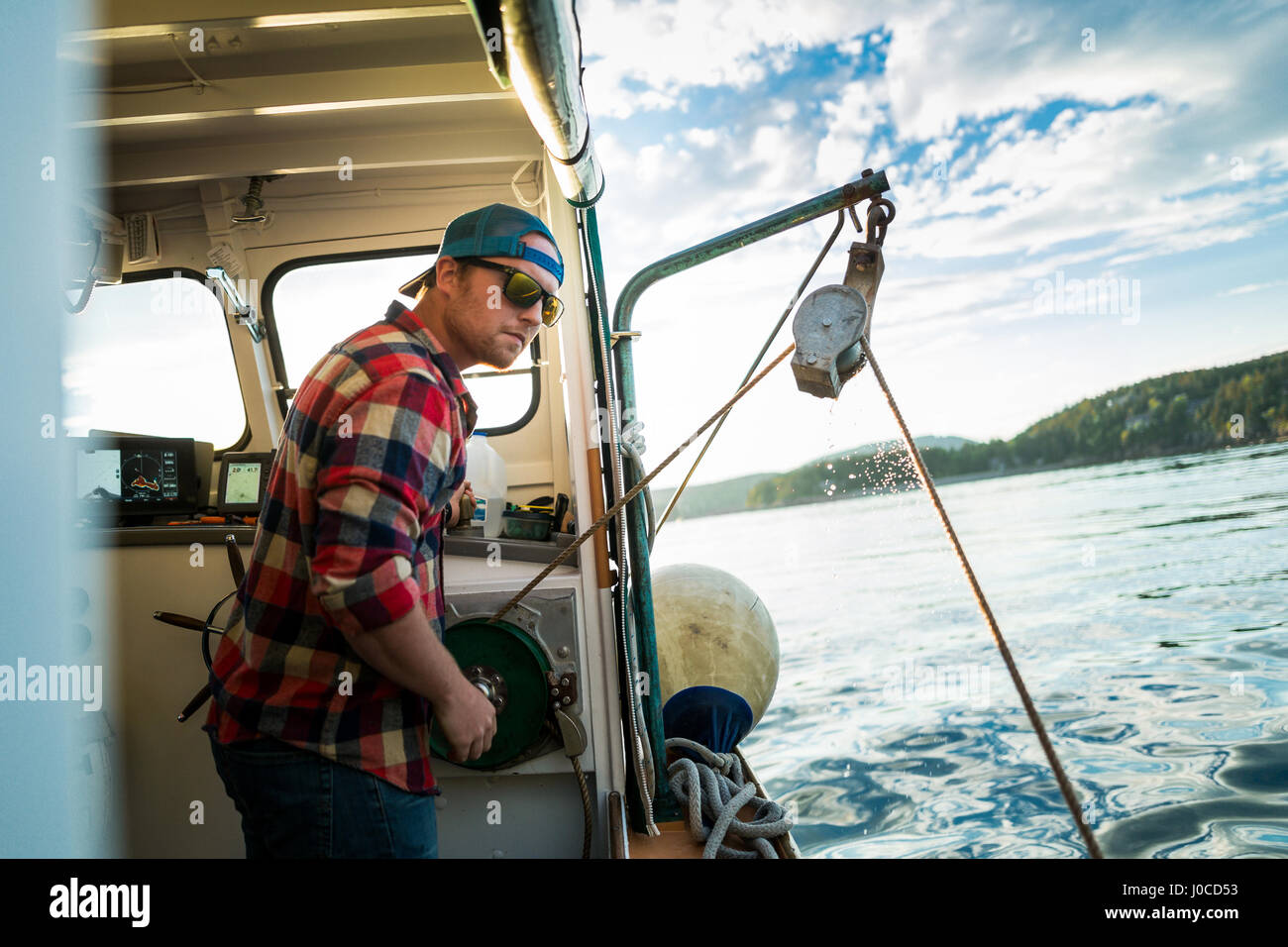 Young man raising winch on fishing boat on coast of Maine, USA Stock Photo