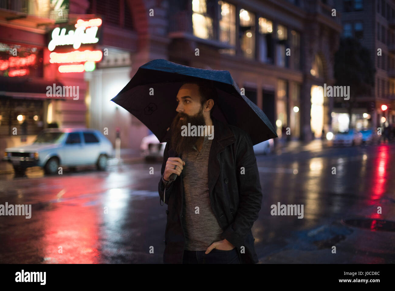 Mid adult man walking in city at night, using umbrella, Downtown, San Francisco, California, USA Stock Photo