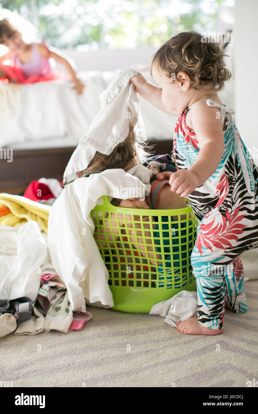 Female toddler removing laundry from child hiding in laundry basket