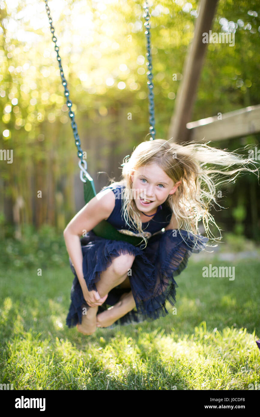 Portrait of girl crouching while swinging on garden swing Stock Photo