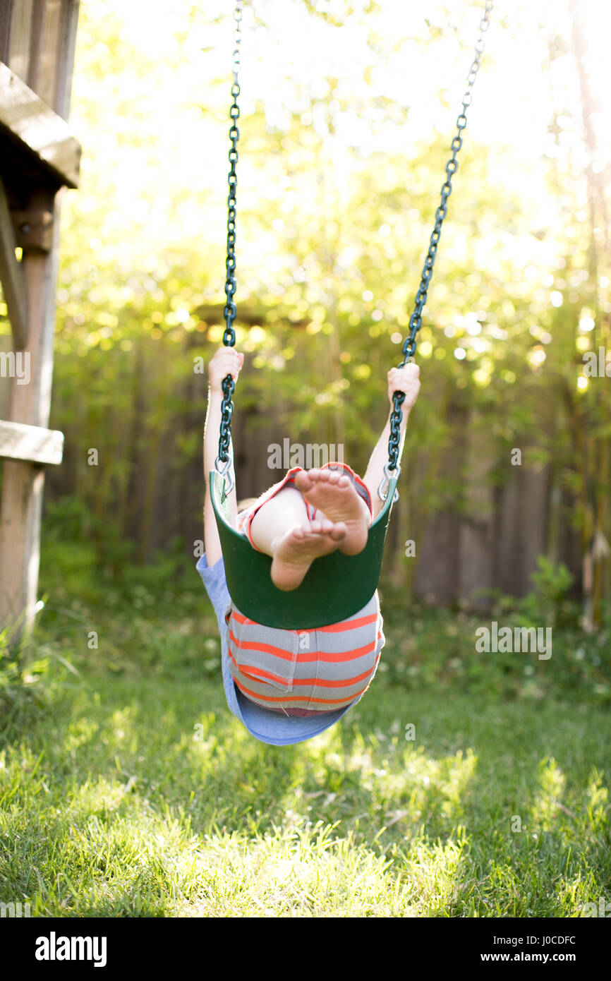 Boy upside down swinging on garden swing Stock Photo