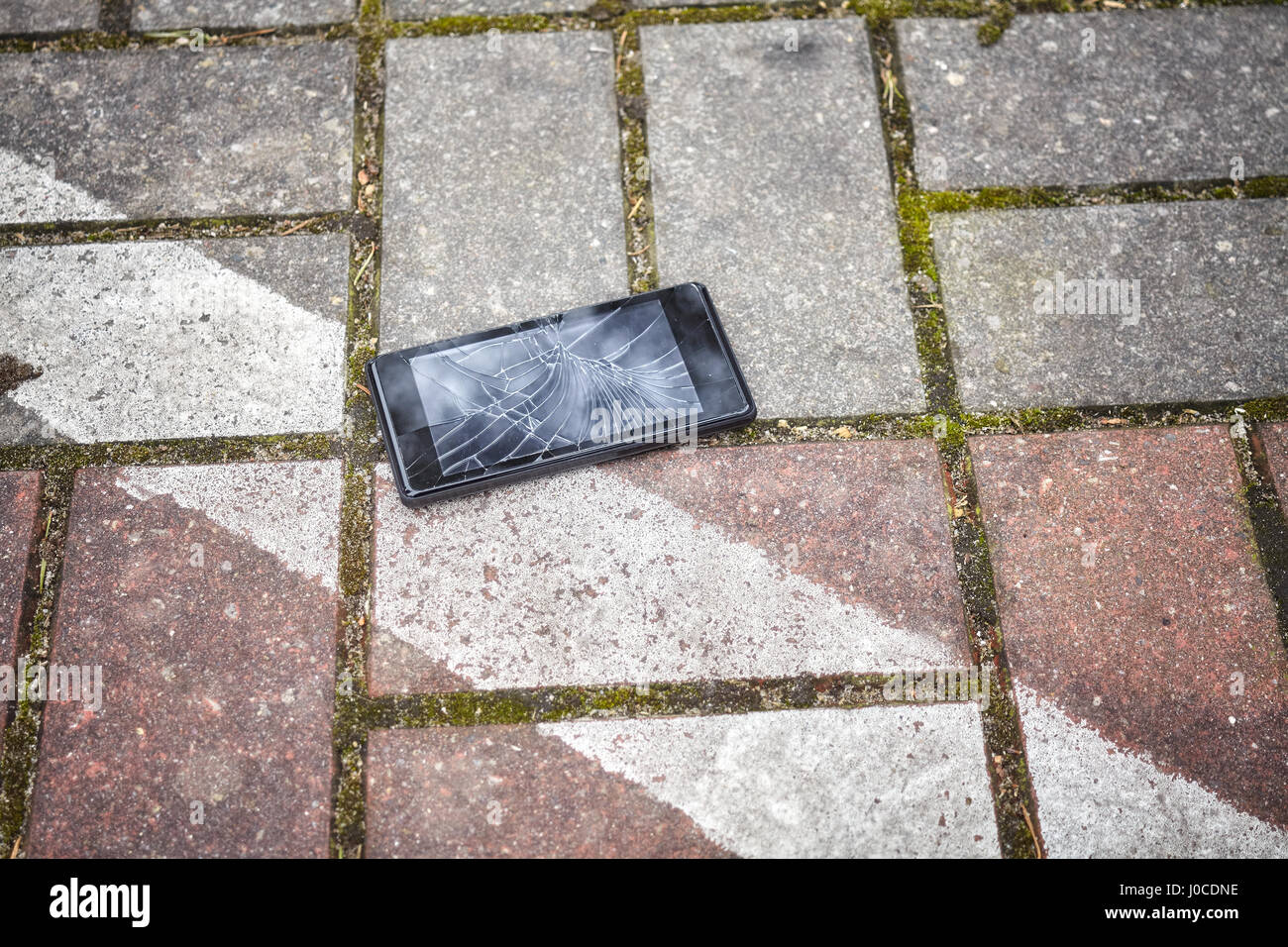 Close up picture of a mobile phone with broken screen on a parking pavement. Stock Photo
