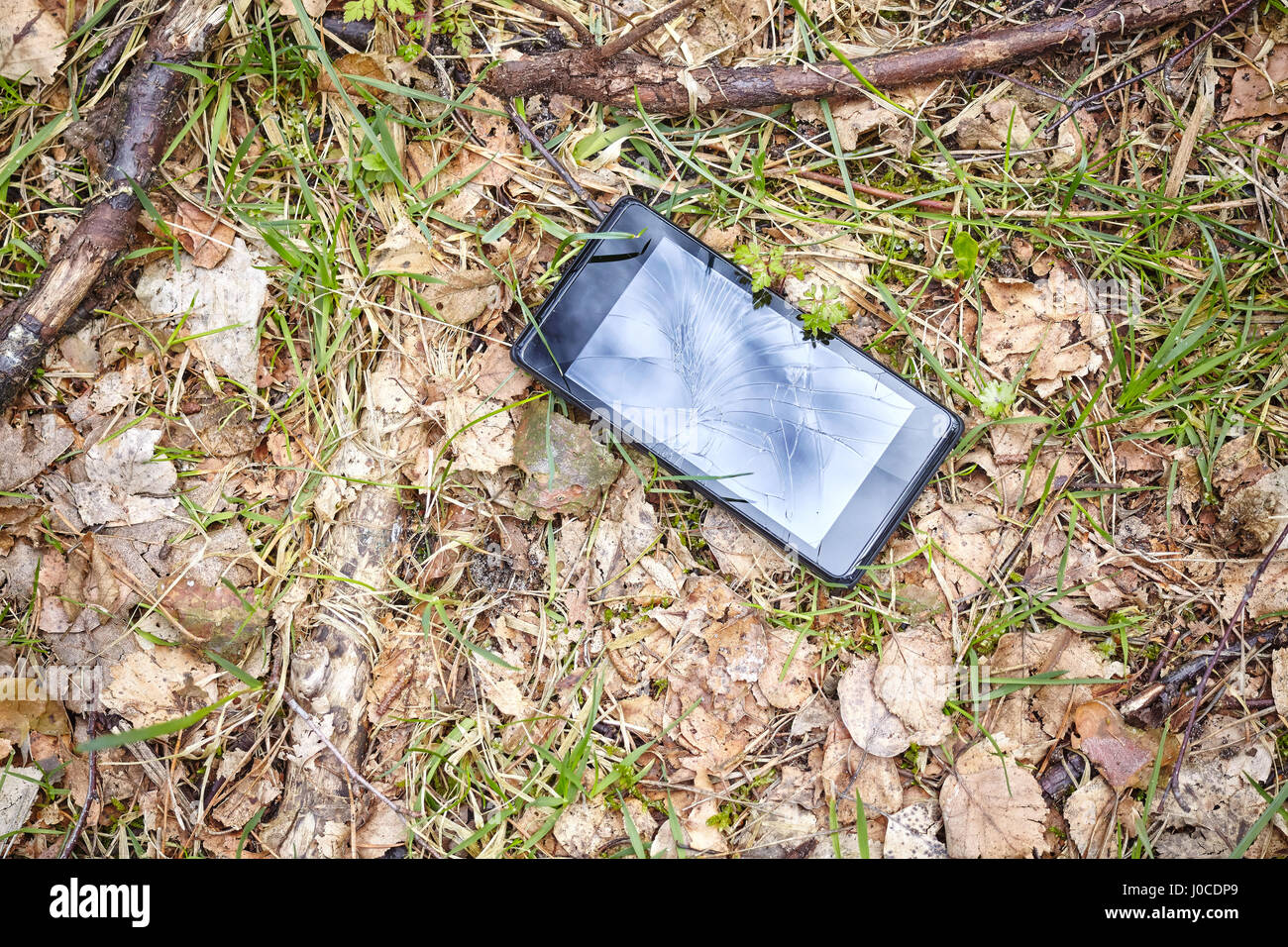 Close up picture of a mobile phone with broken screen on a ground in a park. Stock Photo