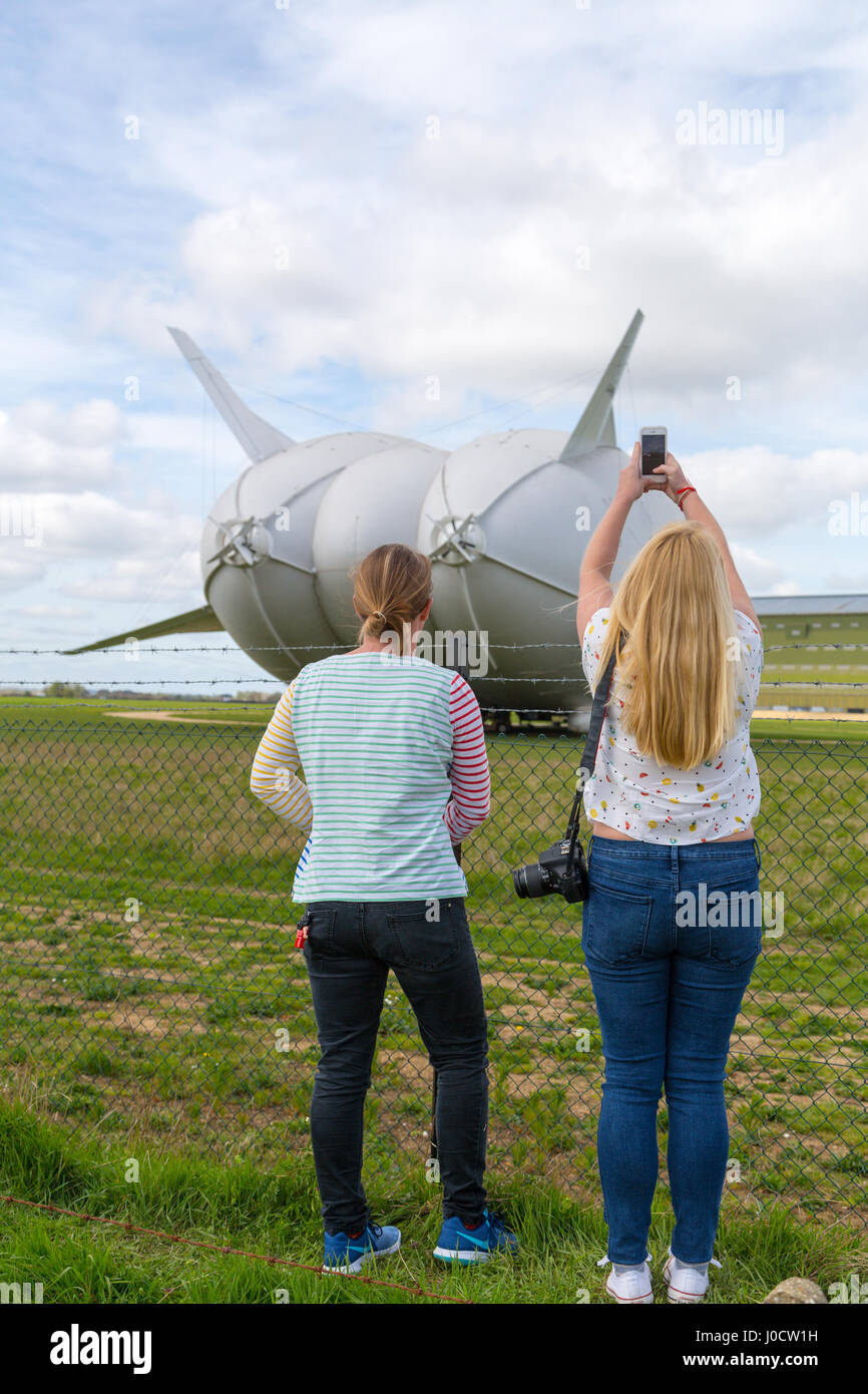 Cardington, Bedfordshire, UK. 11th Apr, 2017. The Hybrid Air Vehicles Airlander 10 is moored to the new Mobile Mooring Mast (MMM), an integrated tracked vehicle and mooring mast, which makes it easier to control and ”push back” the Airlander when manoeuvering it around the airfield. The aircraft is due to begin it's 2017 flight test programme this month. Spectators and photographers wait in anticipation of the first flight. Photo Credit: Mick Flynn/Alamy Live News Stock Photo