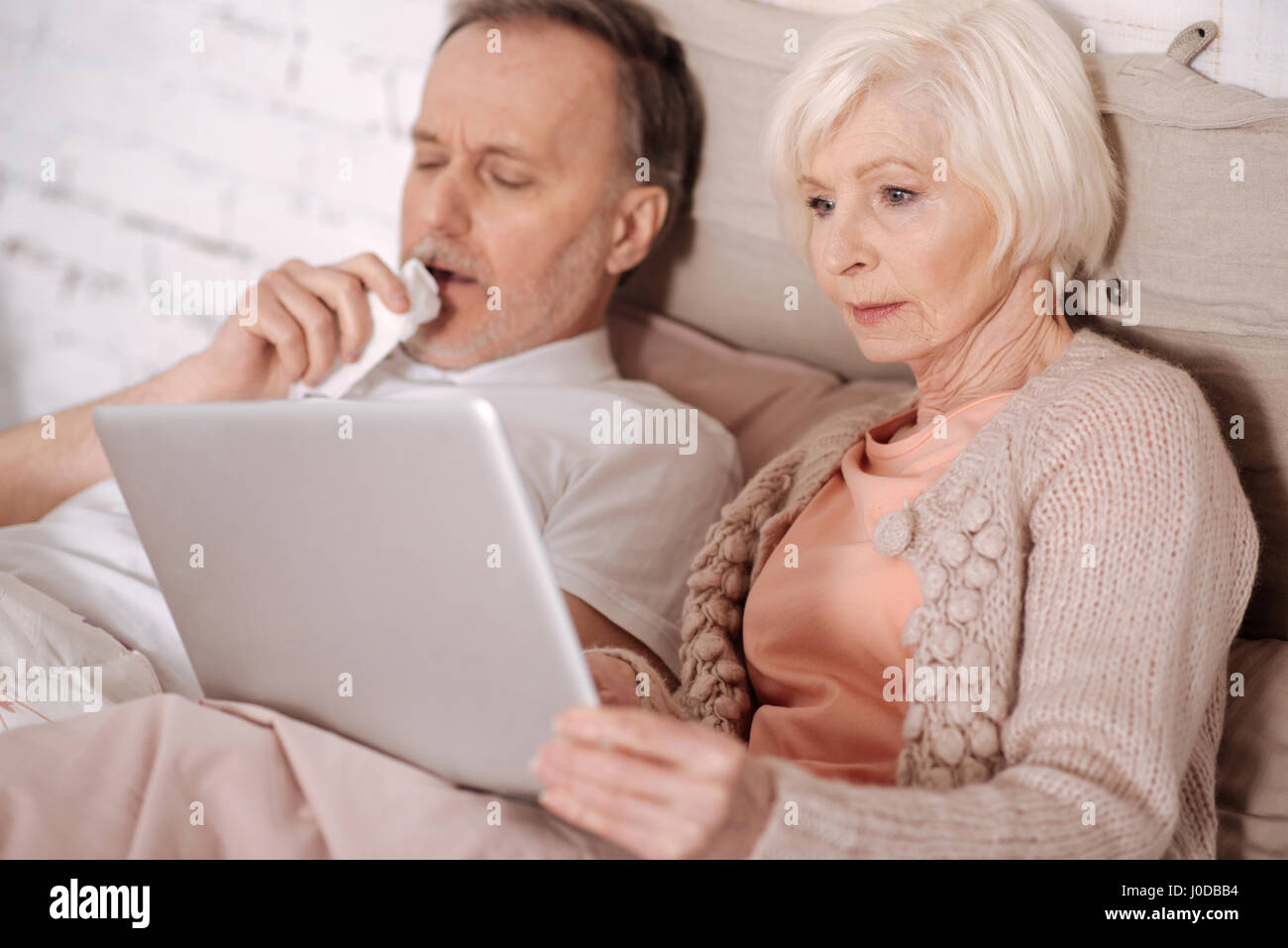 Trying to entertain. Elderly woman lying on bed near her coughing