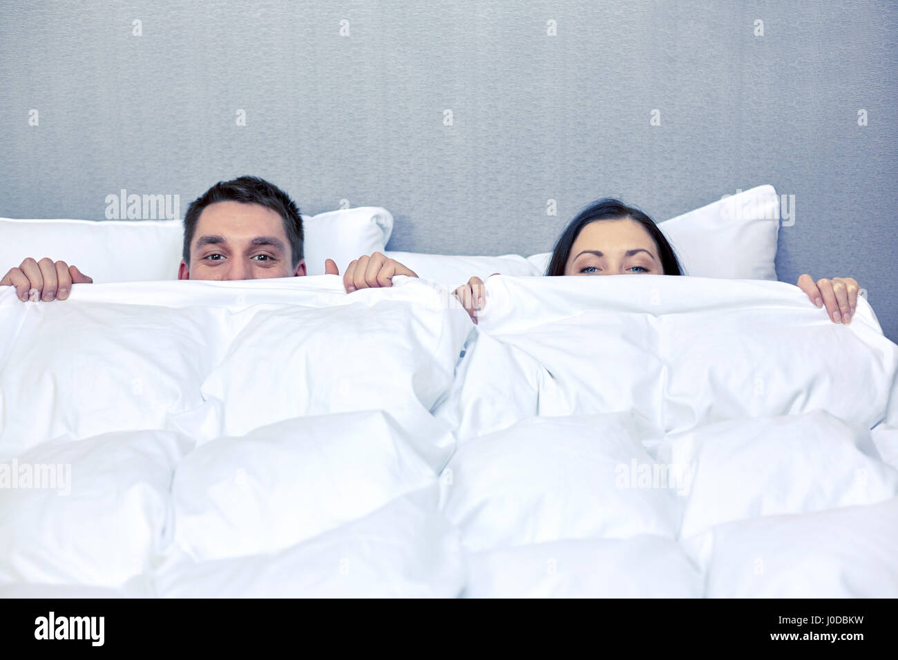 happy couple hiding under blanket in bed Stock Photo Alamy