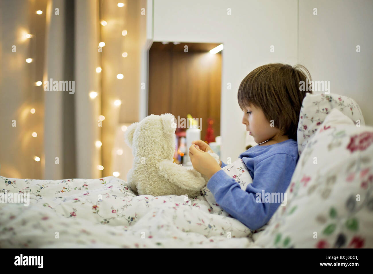 Cute sick child, boy, staying in bed, playing with teddy bear, giving
