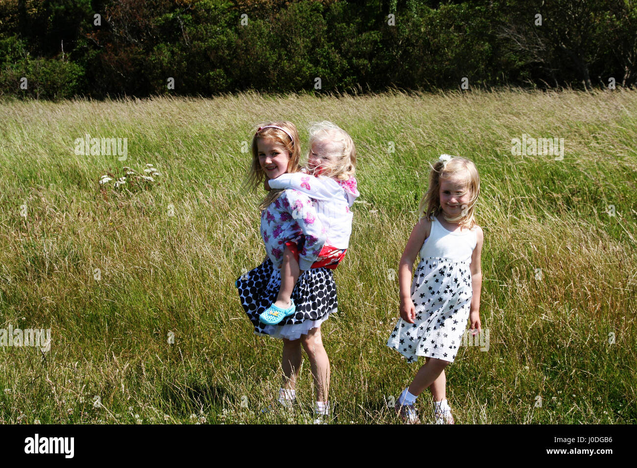 Children playing long grass free sunny summers day with windswept hair and summer dresses, piggyback , piggy back ride Dublin Ireland freedom carefree Stock Photo