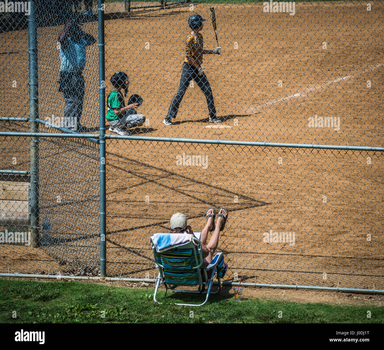 Youth league baseball player at bat. Parent relaxes in lawn chair to