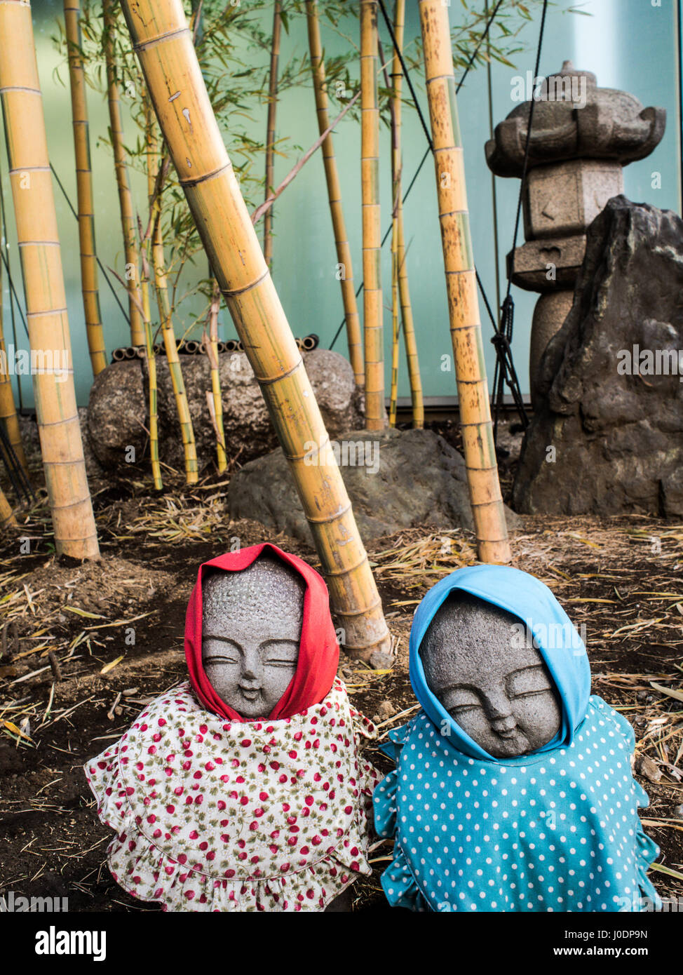 Jizo statues with hoods and bibs, bamboo and ishidoro in the background, at the entrance to a grave yard, Azabu, Tokyo, Japan Stock Photo