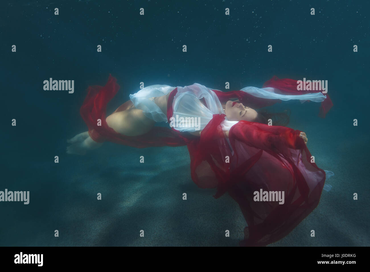 Woman in red dress dancing underwater in the pool. Stock Photo