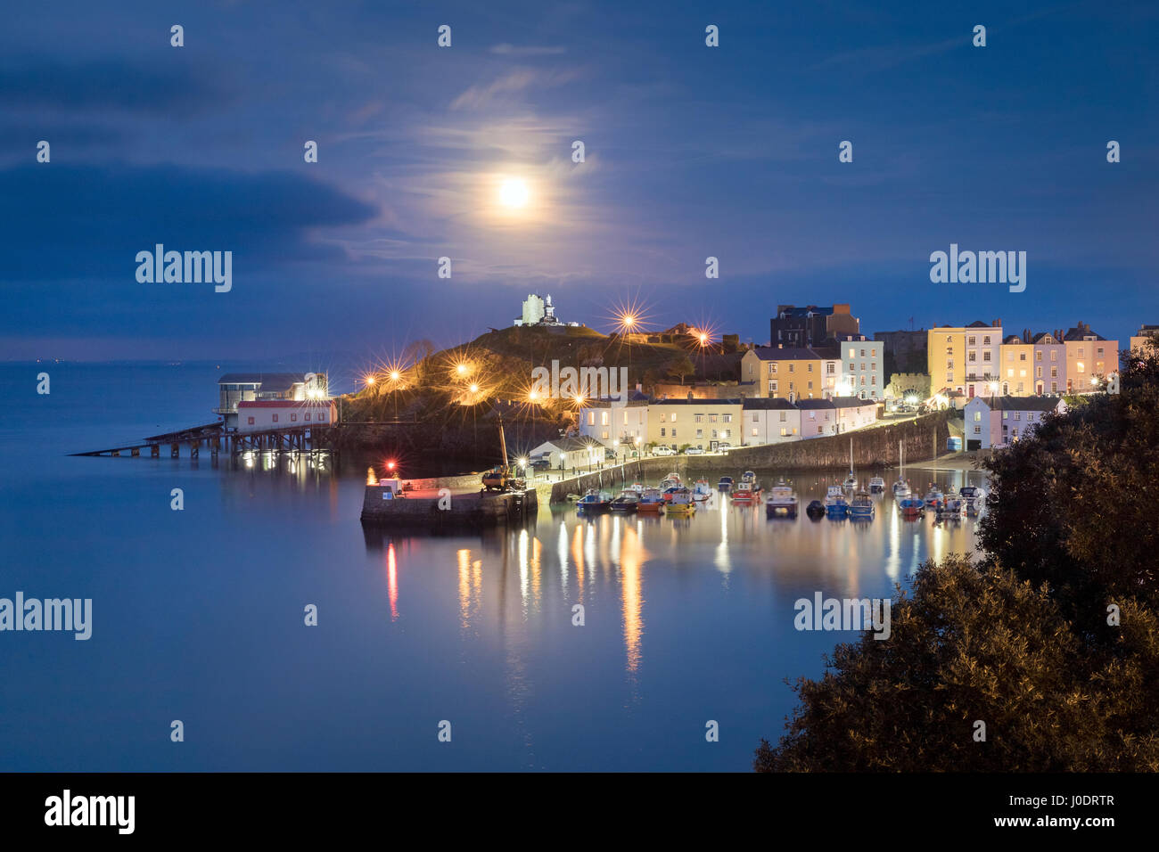 The 'pink' April full moon rises over a serene Tenby Harbour at high tide. Pembrokeshire in Wales Stock Photo