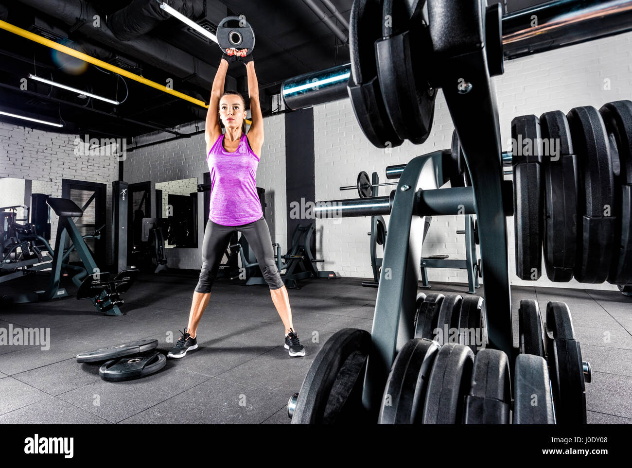 Athletic young woman doing exercise with barbell plate in gym Stock ...