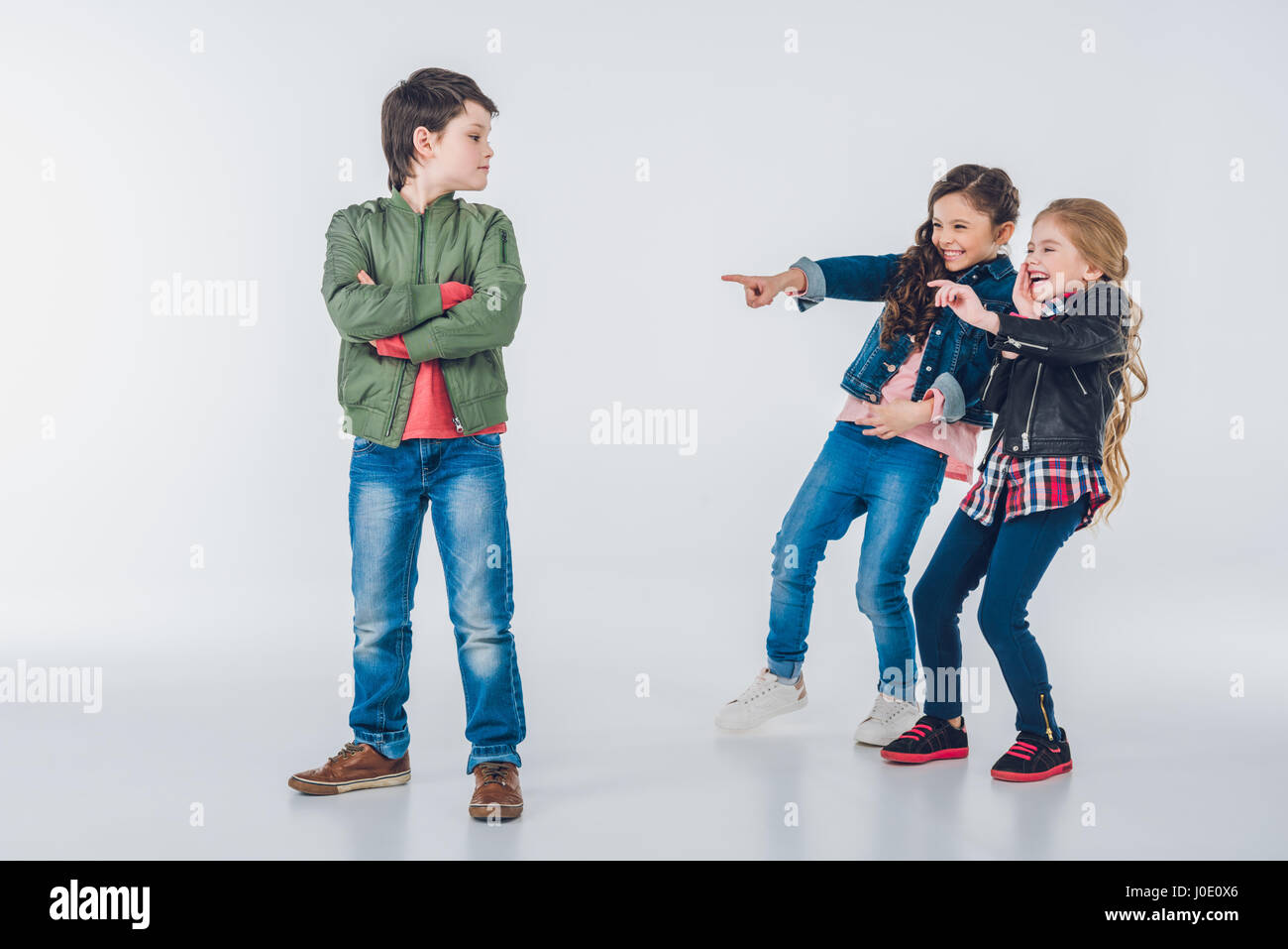 Girls making fun of proud boy and pointing with fingers on grey Stock