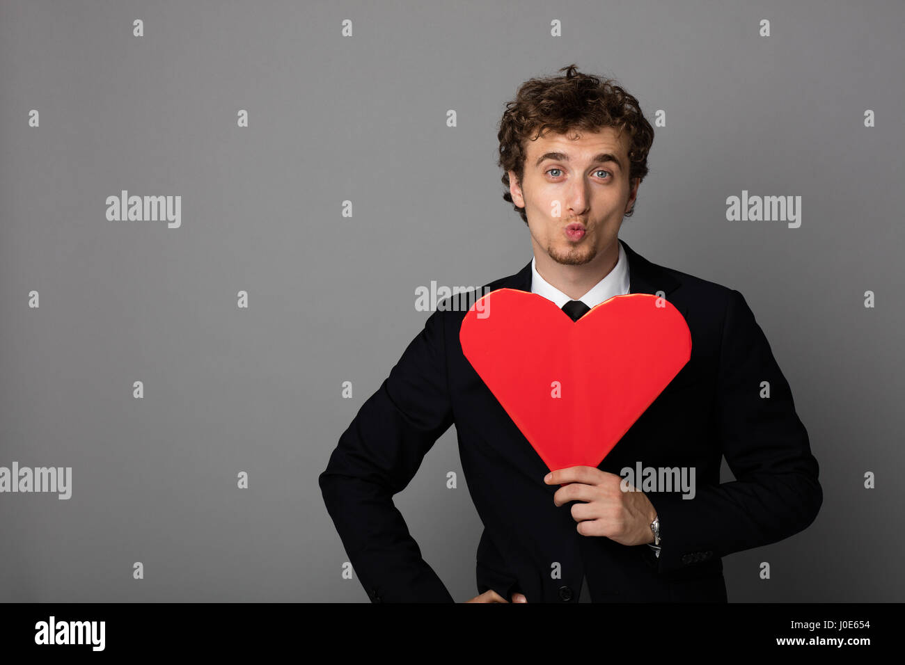 handsome curly man in elegant suit holding a heart in hands and smiling ...