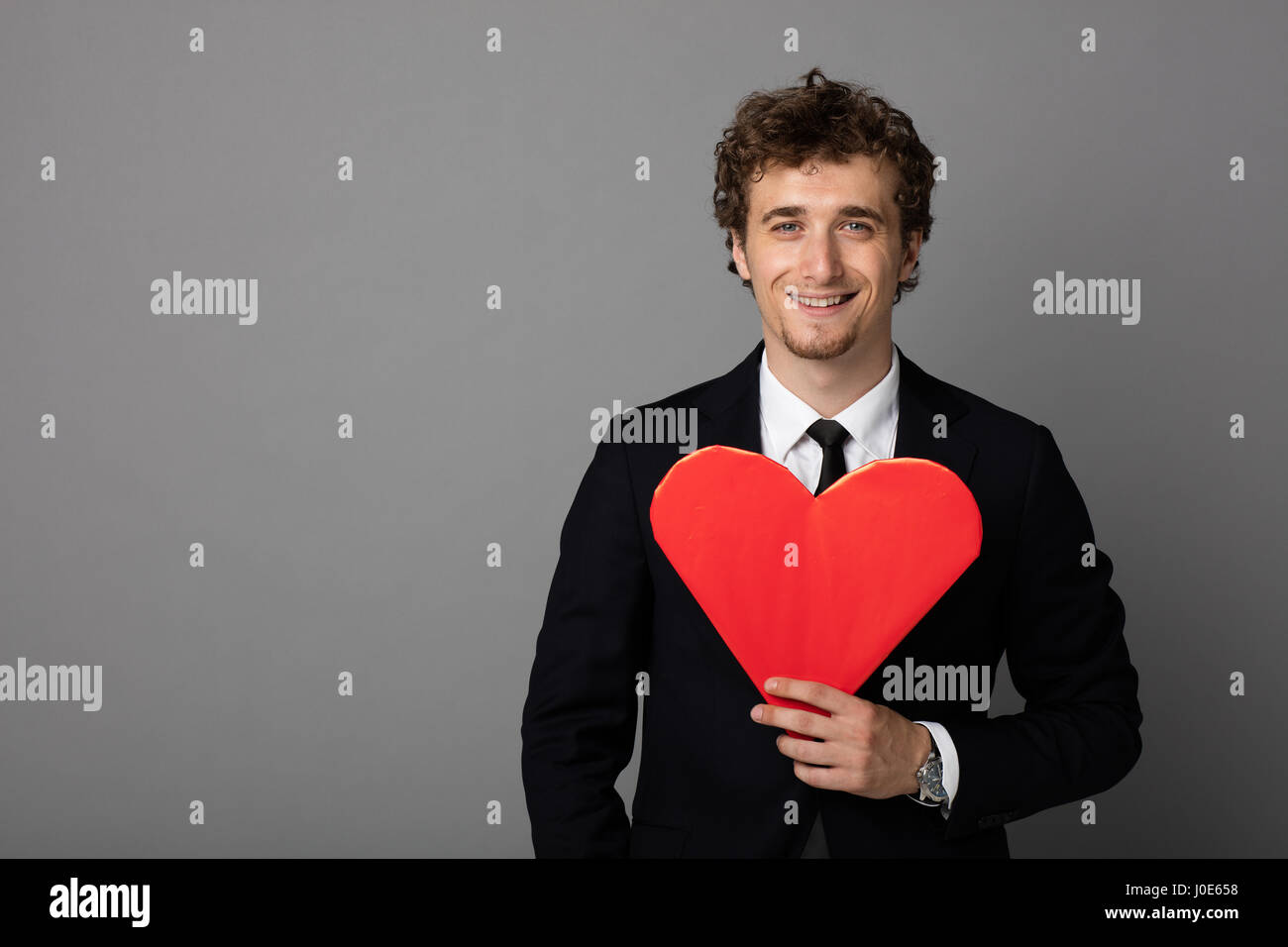 handsome curly man in elegant suit holding a heart in hands and smiling ...