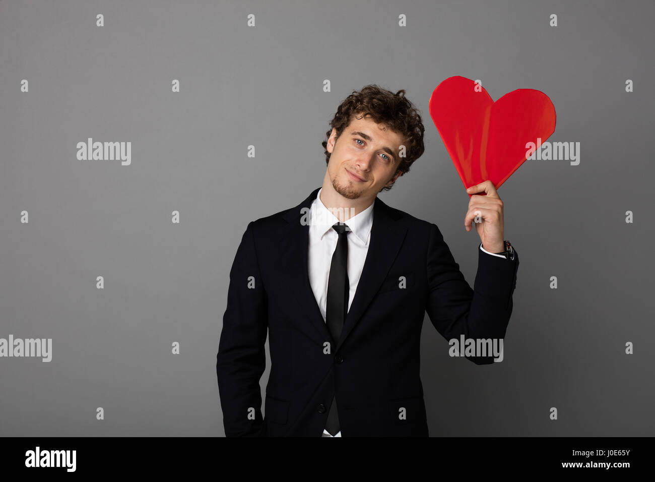 handsome curly man in elegant suit holding a heart in hands and smiling ...