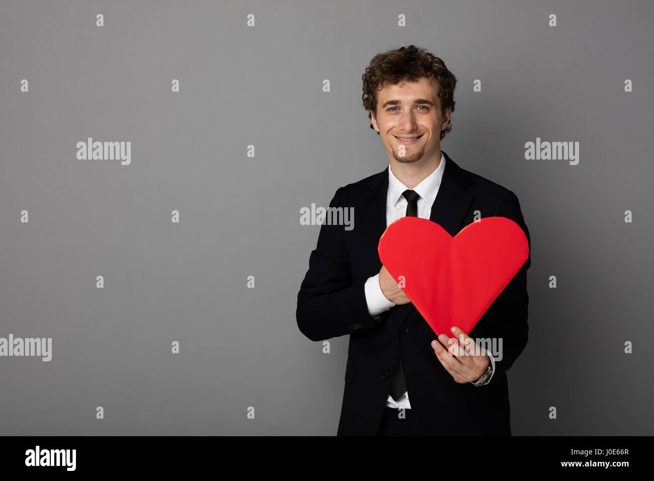 handsome curly man in elegant suit holding a heart in hands and smiling ...