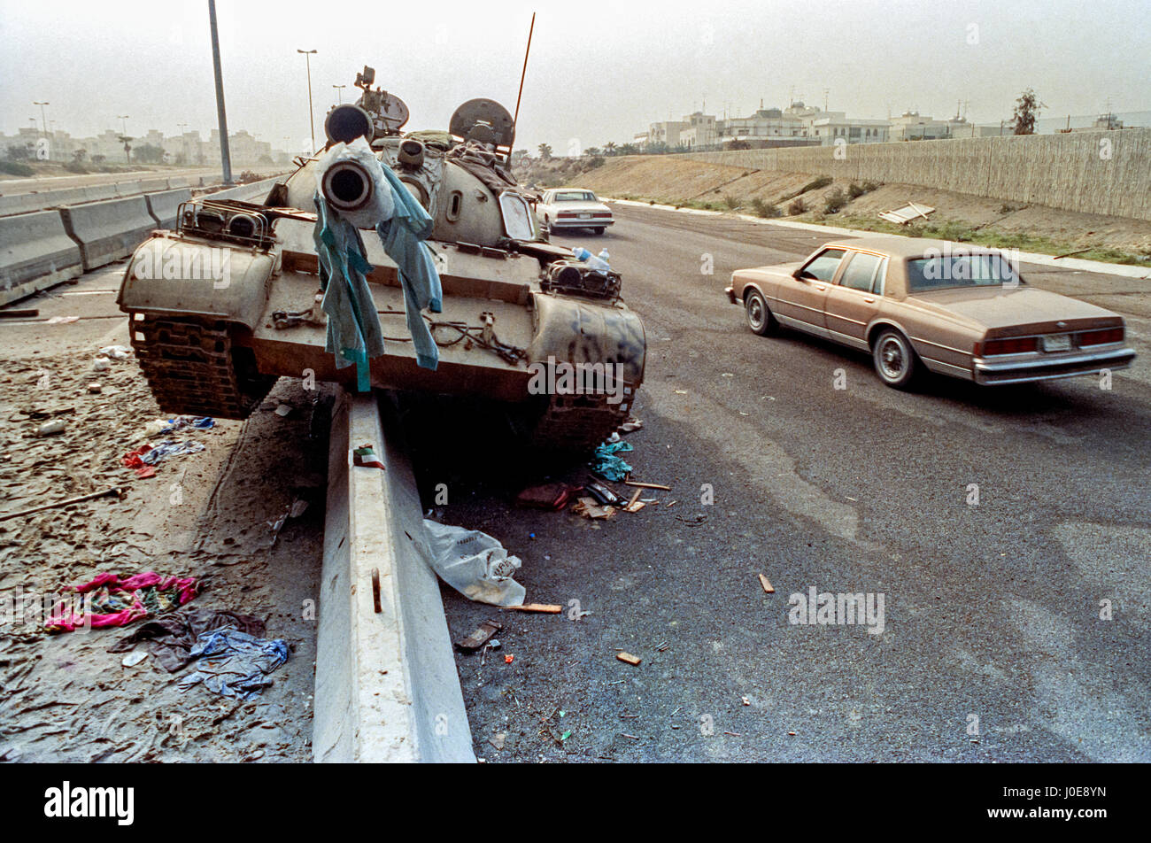 Cars drive past a destroyed Iraqi Army T-72 tank left behind by retreating soldiers following the liberation of Kuwait March 1, 1991 in Kuwait City, Kuwait. After four days of fighting, all Iraqi troops were expelled from Kuwait, ending a nearly seven-month occupation of Kuwait by Iraq. Stock Photo
